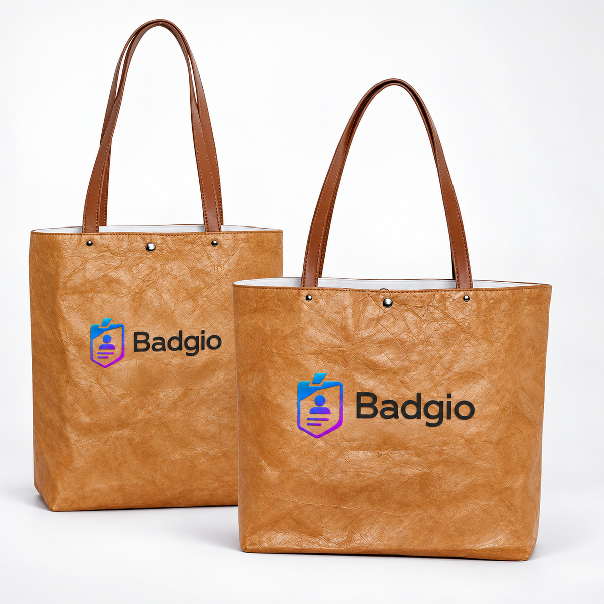 Two tan washable paper tote bags with handles and Badgio logo